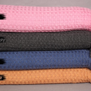 May include: Four fabric swatches stacked on top of each other. The top swatch is pink, the second is dark gray, the third is navy blue, and the bottom swatch is orange. The swatches are all textured and have a waffle-like pattern.