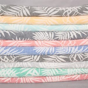 May include: A stack of ten towels with a white leaf pattern on a variety of colored backgrounds. The colors are dark green, mustard, mint, navy, coral, sax blue, black, light gray, green, and red.