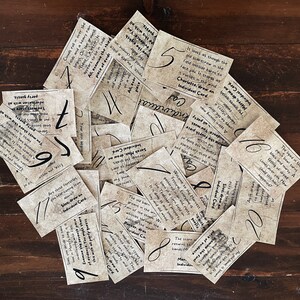 Puede incluir: Una pila de tarjetas de papel marr&oacute;n con texto escrito a mano y n&uacute;meros en ellas. El texto incluye frases como "Ama como si el espantap&aacute;jaros viejo en el campo estuviera all&iacute; para enfrentarte", "Bienvenido al bosque" y "Las estrellas sugieren un regreso a las viejas manos".