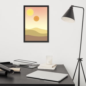 May include: A framed print of a desert landscape with two yellow suns in the sky. The print is in a black frame and is hanging on a white wall.