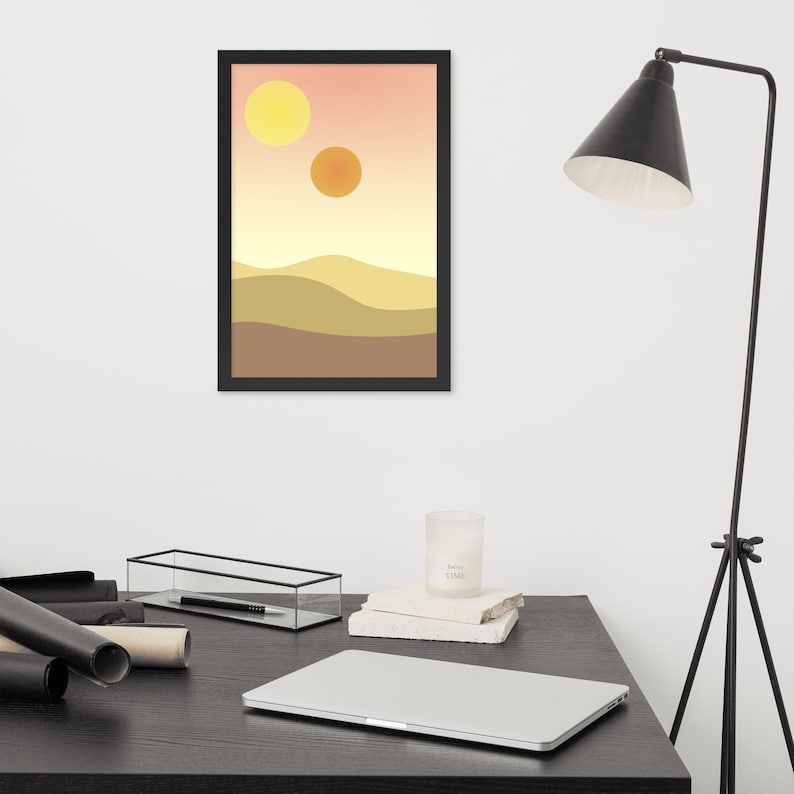 May include: A framed print of a desert landscape with two yellow suns in the sky. The print is in a black frame and is hanging on a white wall.