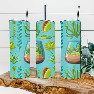 May include: Three stainless steel tumblers with a blue background and a pattern of green plants and succulents. The tumblers have lids and straws.