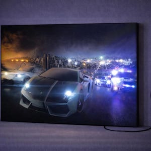 May include: A rectangular wall art print featuring a high-speed night scene with a silver sports car in the foreground, illuminated by bright headlights. The background shows a city skyline and a police vehicle with flashing blue and white lights.
