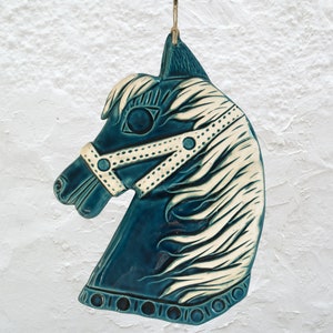 Puede incluir: Cabeza de caballo de cerámica azul turquesa con detalles blancos. El caballo tiene una crin blanca y una brida blanca con lunares blancos.