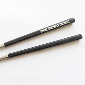 Puede incluir: Una taza de cerámica blanca con un asa negra y el texto "But First, Coffee" en negro, con una fuente de estilo manuscrito. La taza está sobre una superficie blanca.