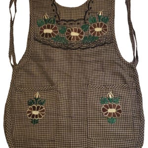 Puede incluir: Delantal a cuadros marr&oacute;n y negro con detalles florales bordados. Cuenta con dos bolsillos y bordados florales decorativos en el peto. El delantal tiene cintas para atar a la cintura y al cuello.
