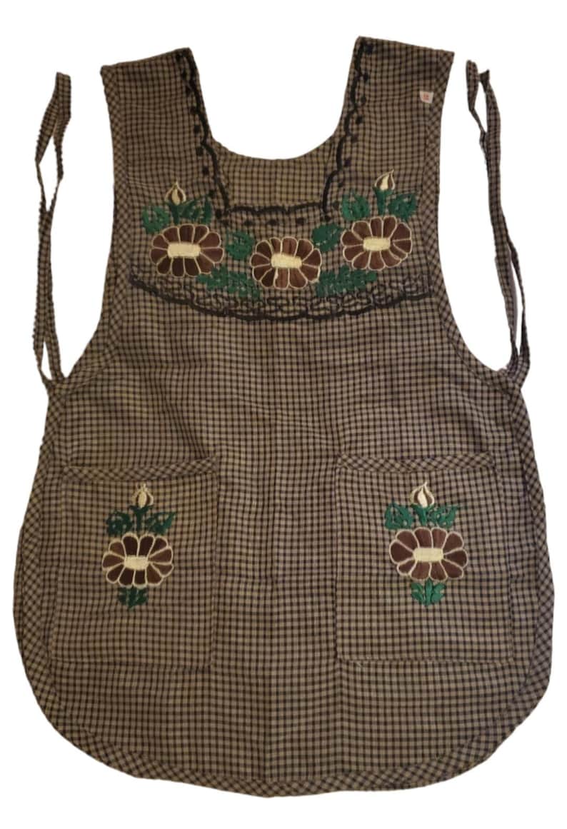 Puede incluir: Delantal a cuadros marr&oacute;n y negro con detalles florales bordados. Cuenta con dos bolsillos y bordados florales decorativos en el peto. El delantal tiene cintas para atar a la cintura y al cuello.