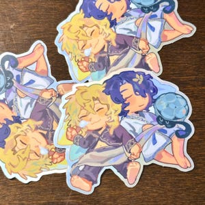 May include: Three colorful stickers featuring cartoon characters with blonde and purple hair. The characters are wearing white and blue clothing and have a whimsical, fairy-like aesthetic.