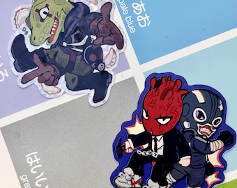 May include: Two die-cut stickers featuring stylized characters. The top sticker shows a green reptilian figure in a dark outfit. The bottom sticker depicts a red heart-headed character in a suit and a blue-masked character with white accents.