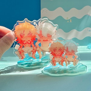 以下が含まれることがあります： オレンジと白の髪の毛をしたアニメ風のキャラクターがベンチに座っている透明なアクリルフィギュア。フィギュアには赤いアクセントがあり、青い雲型のベースに取り付けられています。背景は波模様の淡い青色です。