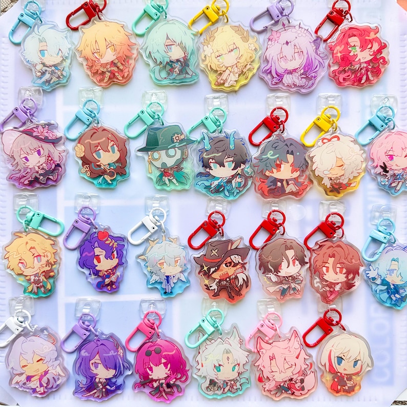 May include: Collection of colorful acrylic keychains featuring anime-style characters. Each keychain has a unique character design with vibrant colors and attached with a metal clasp. The keychains are displayed on a white surface.