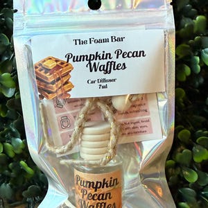 Puede incluir: Un ambientador para coche en una bolsa de pl&aacute;stico transparente. La etiqueta dice "The Foam Bar Pumpkin Pecan Waffles Car Diffuser 7ml". El peque&ntilde;o frasco de vidrio tiene una tapa de madera y una etiqueta que dice "Pumpkin Pecan Waffles".