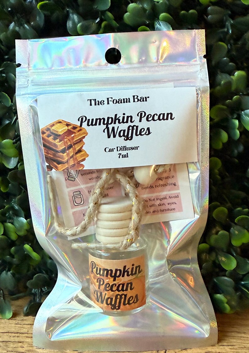 Puede incluir: Un ambientador para coche en una bolsa de pl&aacute;stico transparente. La etiqueta dice "The Foam Bar Pumpkin Pecan Waffles Car Diffuser 7ml". El peque&ntilde;o frasco de vidrio tiene una tapa de madera y una etiqueta que dice "Pumpkin Pecan Waffles".