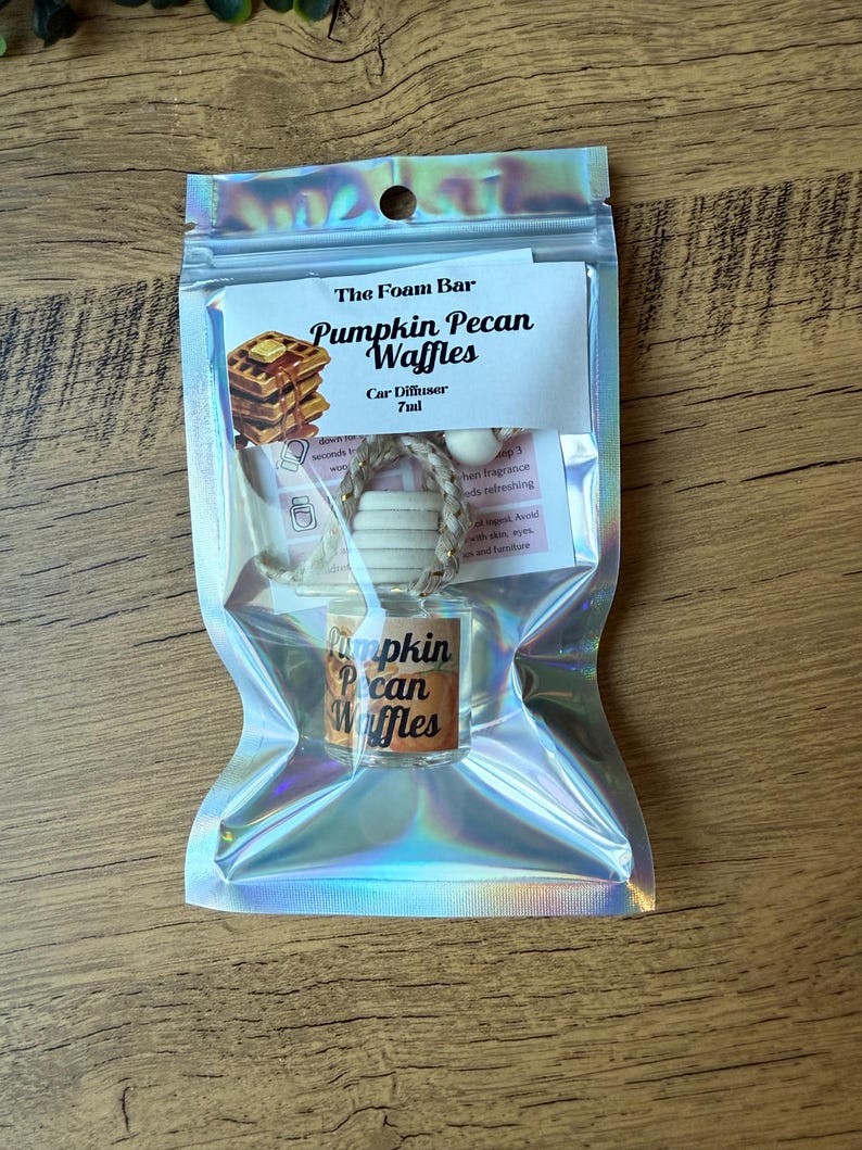 Puede incluir: Un ambientador para coche en una bolsa hologr&aacute;fica. La etiqueta dice "Pumpkin Pecan Waffles" con una imagen de gofres. El producto incluye un peque&ntilde;o frasco de vidrio y un difusor de madera. La bolsa est&aacute; sellada y lista para usar.