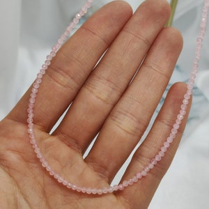 Puede incluir: Delicado collar de cuentas rosas. El collar est&aacute; compuesto por peque&ntilde;as cuentas redondas de color rosa claro ensartadas. Las cuentas est&aacute;n espaciadas uniformemente, creando un dise&ntilde;o sutil y elegante. El collar se muestra sobre un fondo suave y neutro.