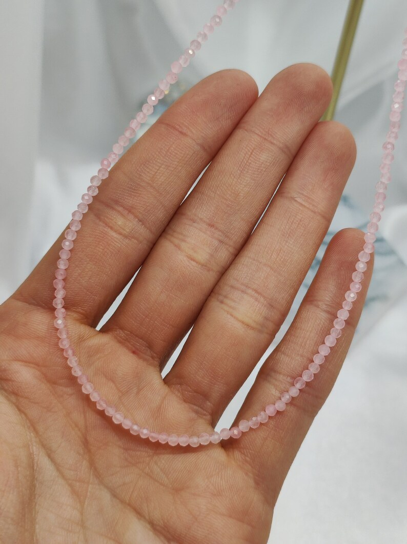 Puede incluir: Delicado collar de cuentas rosas. El collar est&aacute; compuesto por peque&ntilde;as cuentas redondas de color rosa claro ensartadas. Las cuentas est&aacute;n espaciadas uniformemente, creando un dise&ntilde;o sutil y elegante. El collar se muestra sobre un fondo suave y neutro.