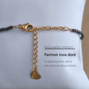 Puede incluir: Primer plano de un cierre y una cadena extensora dorados. El collar presenta peque&ntilde;as cuentas de color gris oscuro. El texto de la imagen dice "Nouvelle option: Fermoir inox dor&eacute;. &Agrave; s&eacute;lectionner dans les options disponibles."