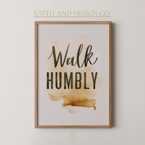Peut inclure: Impression encadrée avec les mots "Walk Humbly" en écriture noire et en lettres majuscules. Le texte est placé sur un fond brun et beige de style aquarelle. Le cadre est en bois clair, et les mots "Faith and Design Co." sont imprimés en haut.