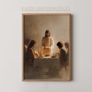Può includere: Una stampa incorniciata di una scena religiosa che raffigura un raduno attorno a un tavolo. L'opera d'arte presenta un'illuminazione soffusa e colori tenui, con figure in abiti fluenti. Il testo "FAITH AND DESIGN CO." è nella parte superiore della cornice.