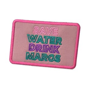 May include: Embroidered patch with a pink background and a hot pink border. The text "SAVE WATER DRINK MARGS" is embroidered in pink, teal, and purple. The patch is rectangular and has a textured appearance.