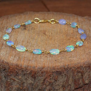 May include: A gold bracelet with oval opals. The opals are in shades of blue, green, and white, strung together with gold wire. The bracelet is fastened with a gold clasp. The bracelet's length is approximately 18 cm.