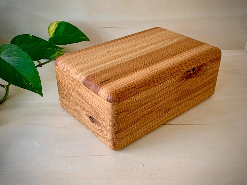 May include: A rectangular wooden box with a natural light brown grain pattern and rounded edges. The box features visible wood knots on the front and top surfaces, showcasing a smooth, polished finish with a distinct, organic texture throughout.