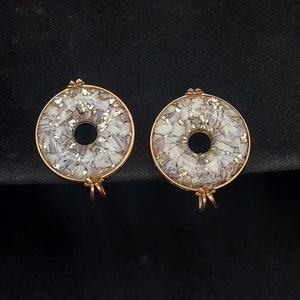 May include: A pair of gold-tone earrings with a white and gold speckled design. The earrings are shaped like a donut with a hole in the center.