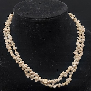 May include: A white shell necklace with multiple strands of small, round beads. The necklace is made of natural materials and has a rustic, organic look.