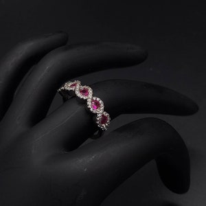 May include: A silver band ring with a row of five ruby stones set in a pave setting. The ruby stones are surrounded by smaller diamonds.