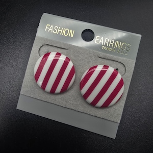 May include: A pair of round, button-style earrings featuring a glossy finish with diagonal magenta and white stripes. The earrings are attached to a grey display card with the text FASHION EARRINGS TAIWAN R.O.C. printed in gold at the top.