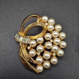 May include: A gold-toned brooch with a cluster of faux pearls and rhinestones in a floral design.