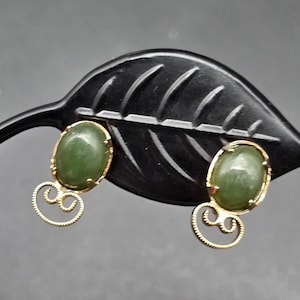 May include: A pair of gold earrings with green oval-shaped stones. The earrings have a delicate, ornate design.