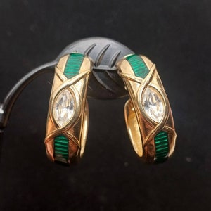 May include: A pair of gold hoop earrings with green enamel and clear rhinestones. The earrings are designed with a criss-cross pattern.