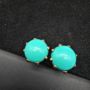 May include: A pair of turquoise blue earrings with gold-toned metal accents. The earrings are round and have a slightly raised center.