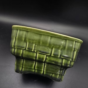 May include: A green ceramic planter with a basket weave design. The planter has a rectangular shape with a slightly angled top and a textured surface. The color is a deep, rich green.