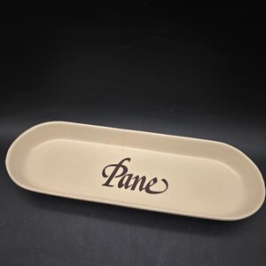May include: An off-white, oval-shaped serving tray with rounded edges. The word "Pane" is written in a dark brown, elegant script across the center. The tray is empty and sits against a dark background.
