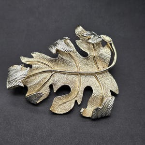 May include: A gold-toned leaf brooch with a textured surface and smaller leaves in silver tone.
