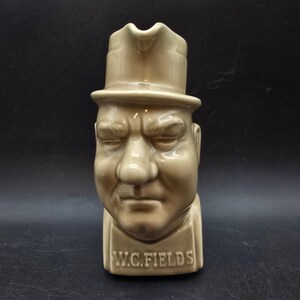 May include: A tan ceramic pitcher in the shape of W.C. Fields' head, wearing a hat. The pitcher has a detailed face with a stern expression. The name "W.C. FIELDS" is printed on the base.