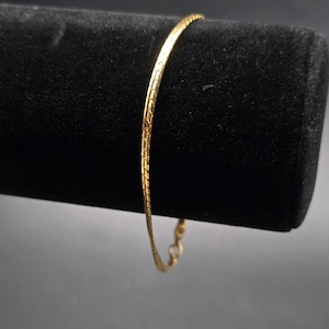 May include: A gold-colored bracelet with a textured, snake-chain design. The bracelet is displayed against a black background, showcasing its delicate and shiny appearance. The bracelet is approximately 7 inches in length.