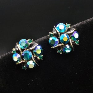 May include: A pair of clip-on earrings with a cluster of iridescent green rhinestones set in gold tone metal.