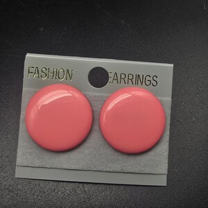 May include: A pair of round, glossy, coral-pink stud earrings attached to a gray display card. The card features the text FASHION EARRINGS printed in gold lettering at the top, with a circular cutout hole positioned between the two words.