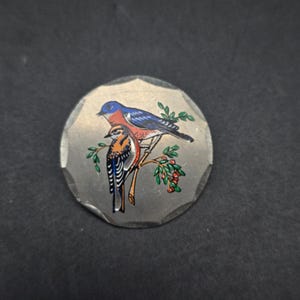 May include: A silver-toned metal pin with a bluebird and a smaller brown bird perched on a branch with red berries. The birds are painted in detail with blue, red, and brown colors.