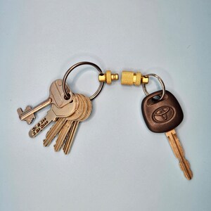 May include: A collection of keys on a black ring, linked to a key with a Toyota logo via a gold-coloured magnetic clasp. The keys are silver metal and are on a black ring.