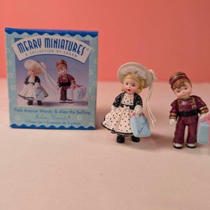 May include: A Merry Miniatures 2-piece set featuring Park Avenue Wendy and Alex the Bellhop figurines. Wendy wears a black and white polka dot dress with a matching hat, holding a blue bag. Alex wears a maroon bellhop uniform, holding a blue gift.