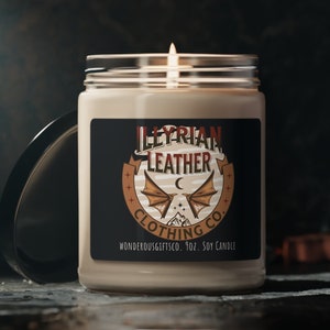May include: A beige soy candle in a glass jar with a black label. The label features a logo with a crescent moon, two bat wings, and the text "Illyrian Leather Clothing Co.  WondrousGiftsCo. 7oz. Soy Candle".