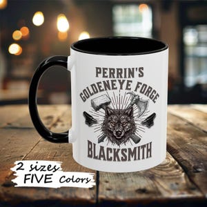 May include: White ceramic mug with a black rim and handle. The mug features a wolf illustration with crossed axes and a hammer. The text "Perrin's Goldeneye Forge Blacksmith" is printed on the mug.