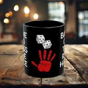 May include: Black coffee mug with white text that reads "Game On Toss The Dice" and a red handprint with two white dice rolling above it.