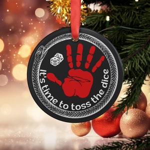 May include: Black and white Christmas ornament with a red handprint and a dice. The ornament has a snake design and the text "It's time to toss the dice".