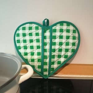 Può includere: Presa pentola a forma di cuore a quadri verdi e bianchi. La presa pentola è trapuntata e ha un anello per appenderla.