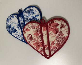 May include: Two heart-shaped quilted pot holders. One is blue and white with a floral pattern, the other is red and cream with a floral and bird pattern. Both have a loop for hanging.